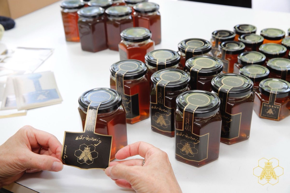 Zürihonig-Gläser mit schwarzem Etikett und goldener Biene werden von Hand etikettiert